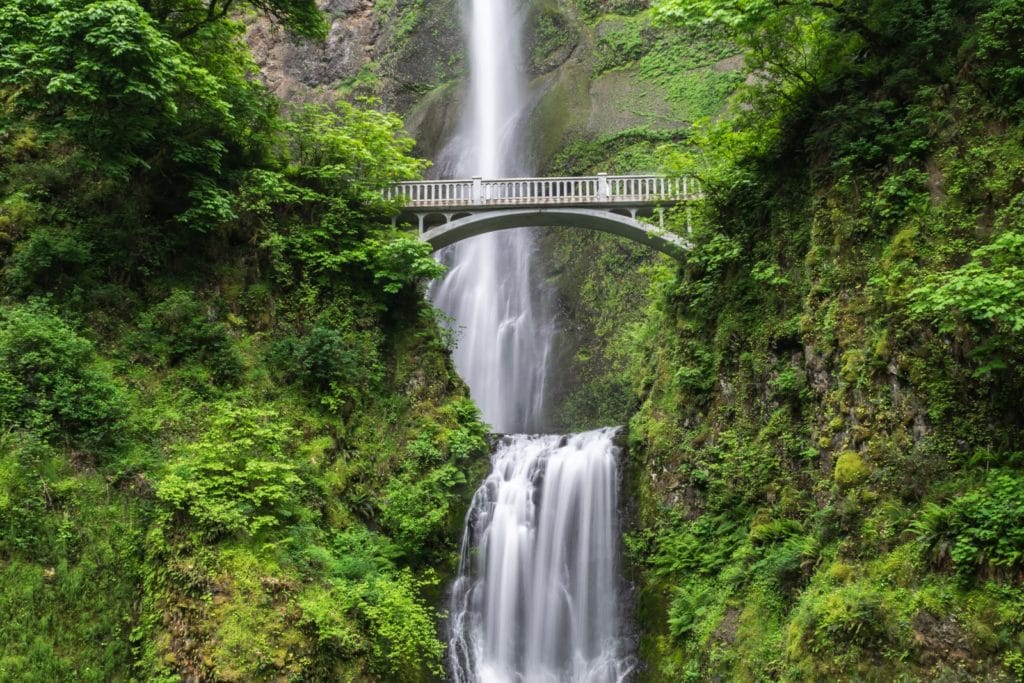 waterfall down green valley with bridge across