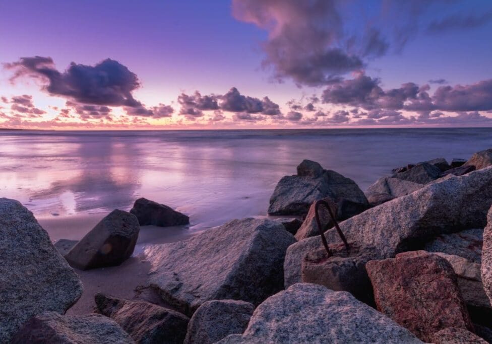 sunset over boulders and water lavender sky